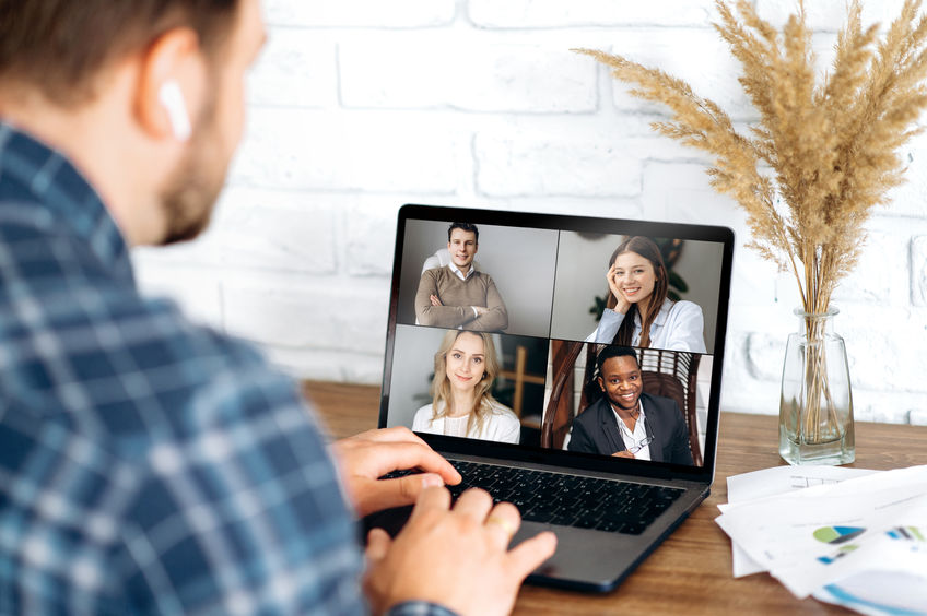 Online business meeting in video conference in the zoom app. A young attractive guy communicates with his colleagues on a video call using a laptop. Distant work at home